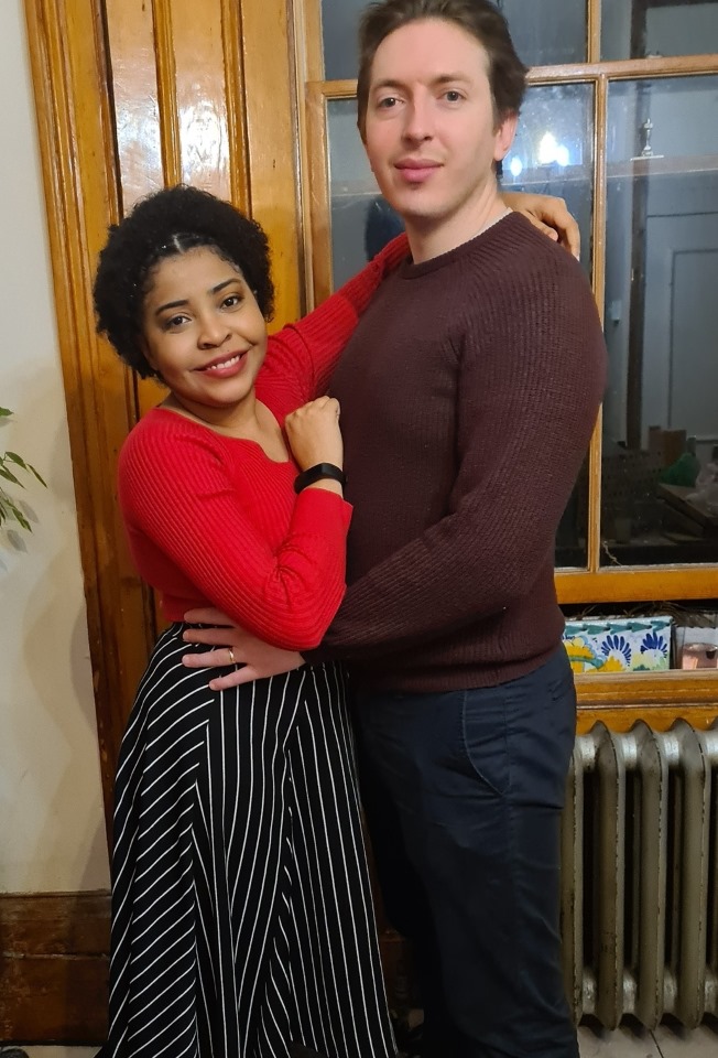 A young couple stand holding each other, smiling for a photo